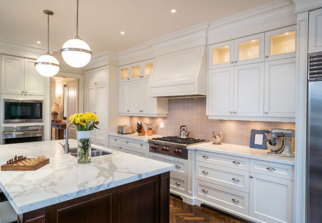 Bright white kitchen with a marble island, pendant lights, and stainless steel appliances.