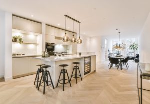 Open-concept kitchen with a marble island, four black bar stools, and hanging pendant lights, leading to a dining area.