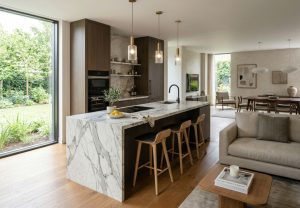 Open-plan kitchen with a marble island and four wooden stools; dark wood cabinetry, pendant lights, and a view of the garden.
