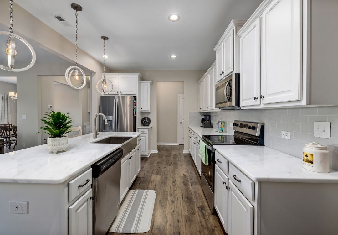 Modern white kitchen with marble island, double sink, and stainless appliances; pendant lights and wood flooring create a bright, open space.